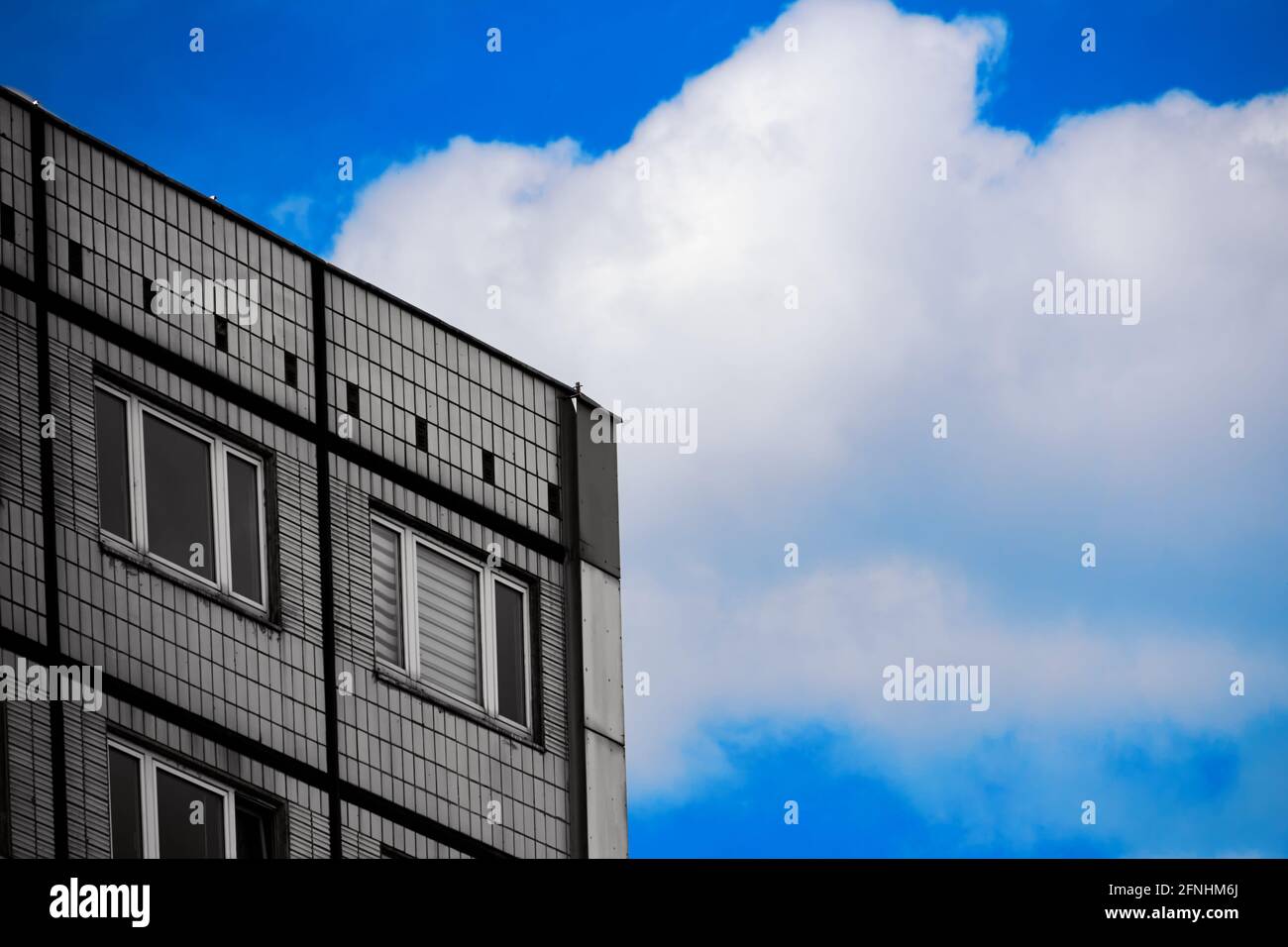 Ecke eines traurigen grauen Fertighauses gegen einen blauen Himmel mit weißer Wolke, abstraktes Minimalismus-Konzept Stockfoto