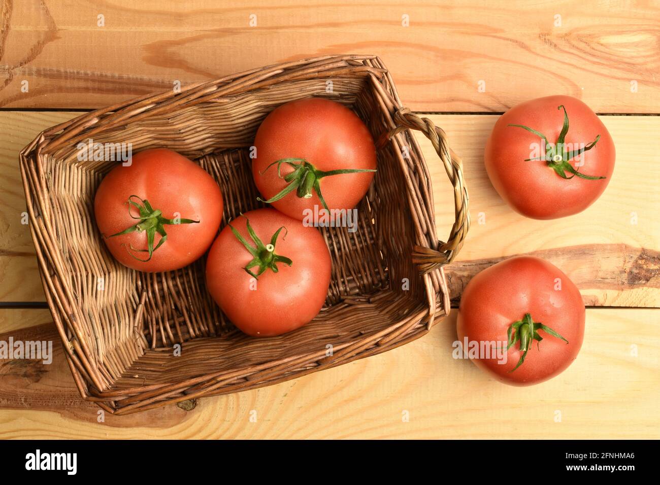 Mehrere reife rosa Tomaten in einem Korb, Nahaufnahme, auf einem Holztisch, Draufsicht. Stockfoto