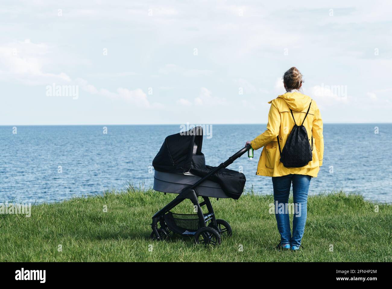 Rückansicht einer Frau im gelben Regenmantel und mit Baby Kinderwagen am Meer Stockfoto