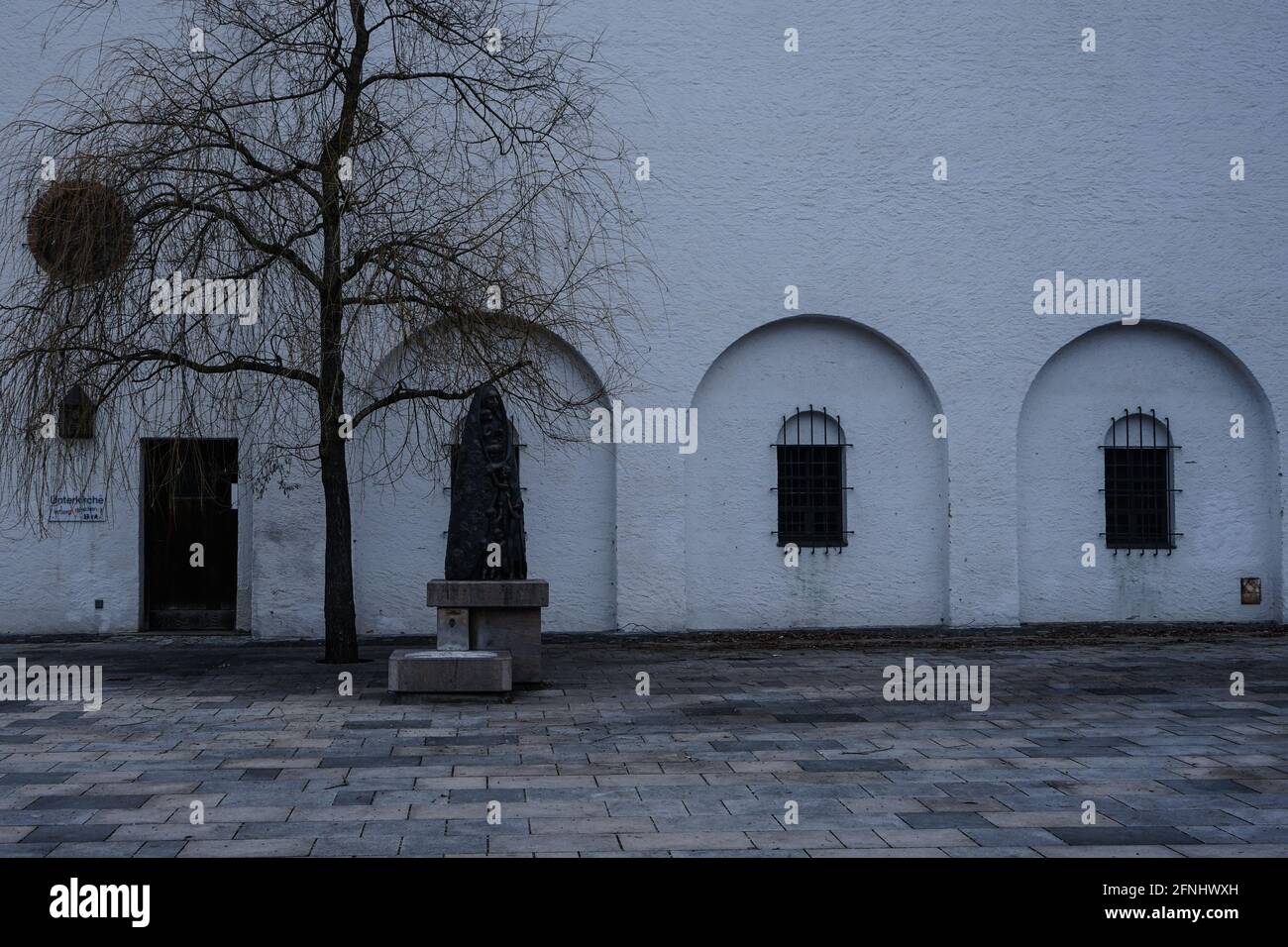 Blick auf eine Kirche mit versperrten Fenstern vor einer Skulptur und einem Baum. Stockfoto