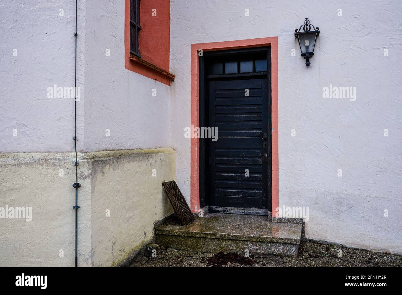 Blick auf eine Eingangstür hinter einer Stufe. Daneben an der Wand eine alte Lampe. Stockfoto