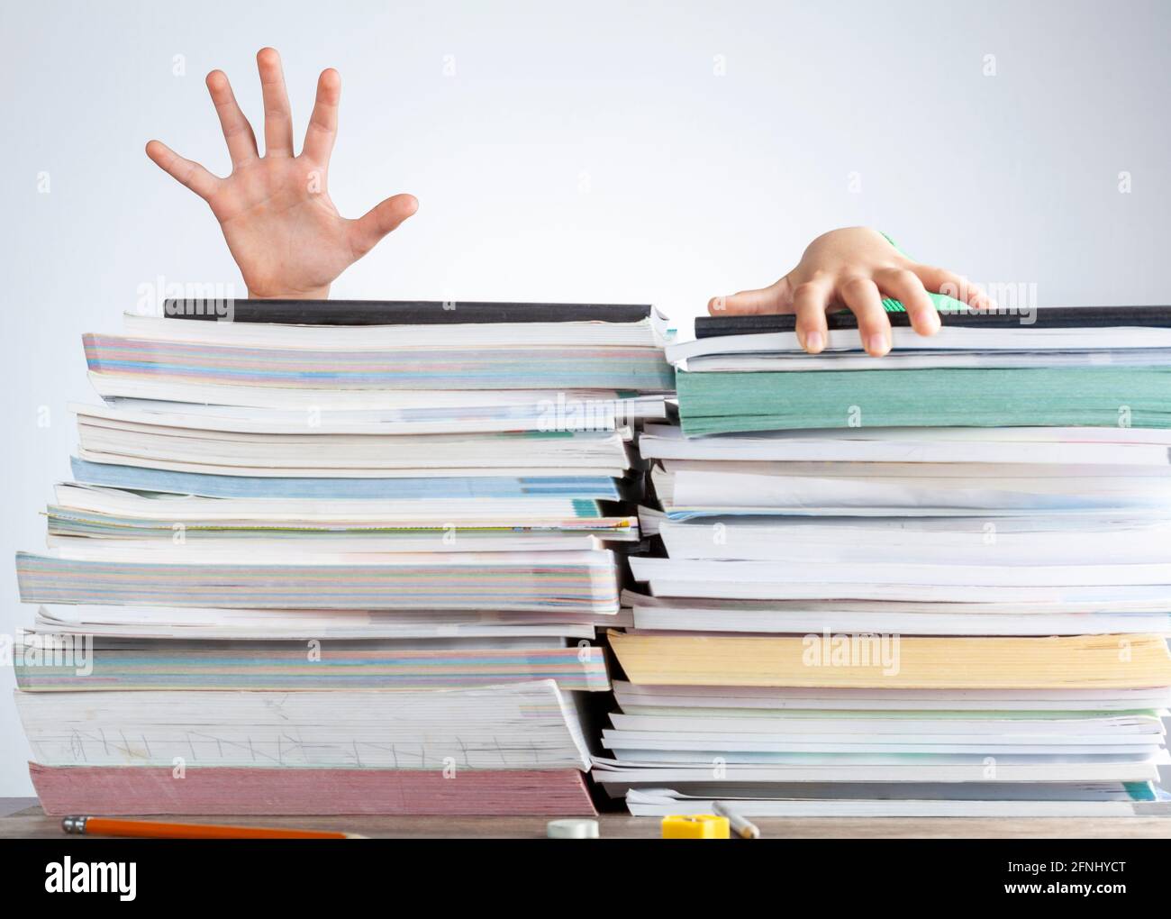 Abstraktes Konzeptbild, das einen jungen Studenten hinter einem großen Stapel von Büchern zur Testvorbereitung auf einem Schreibtisch zeigt. Eine überwältigende Last. Das Kind versucht zu esca Stockfoto