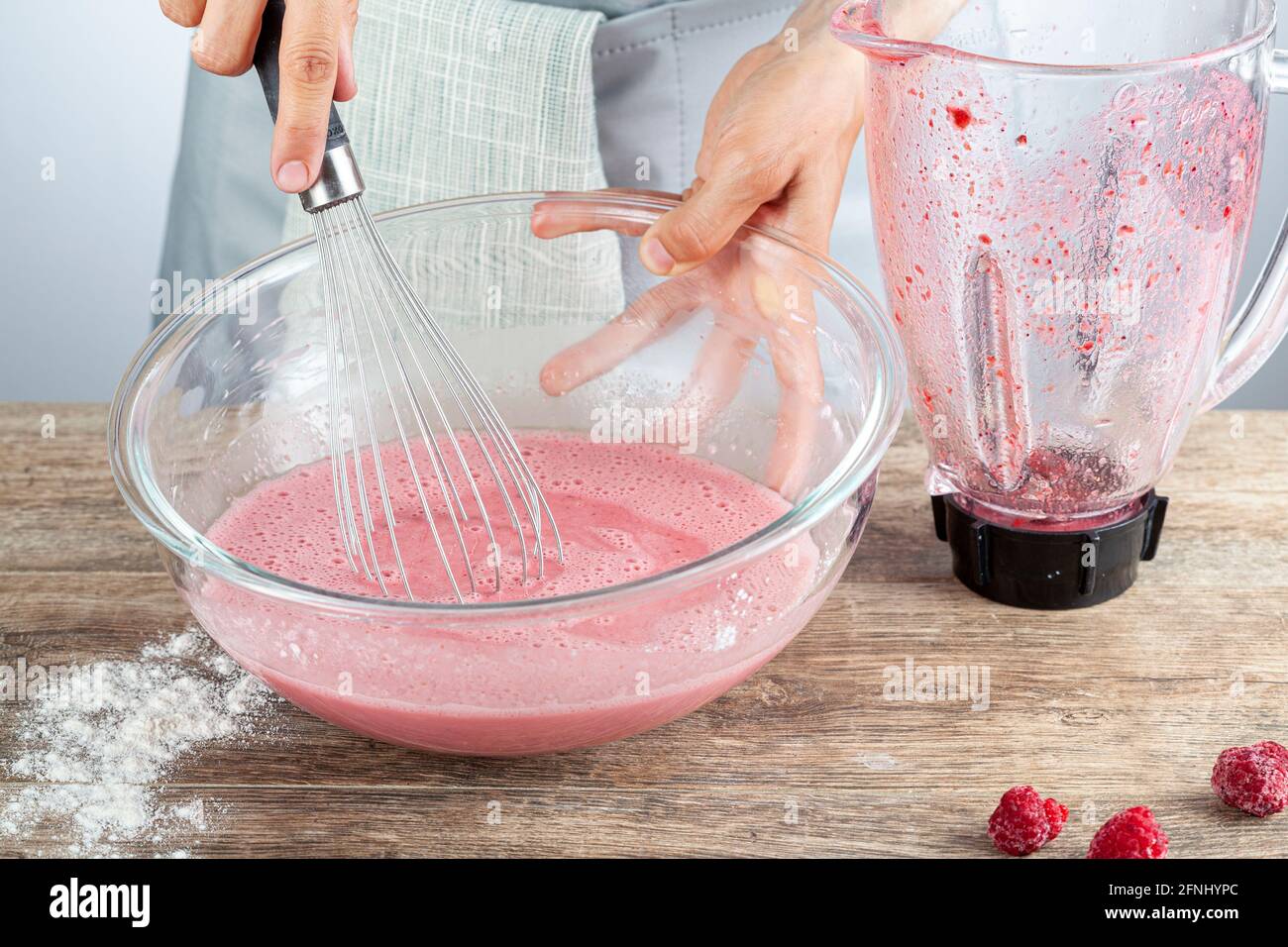 Eine kaukasische Frau mischt einen roten Fruchtsaft aus frischen Beeren in einer Glasschüssel mit einem Schneebesen im Ballon. Vielseitiges Bild für die Zubereitung von Speisen zu Hause Stockfoto