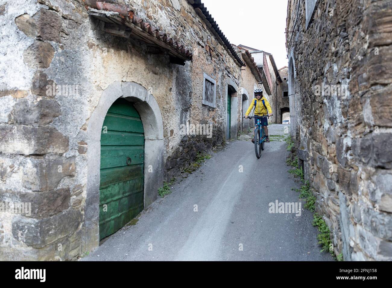 Junge Radfahren in der engen Straße von Goce, kleines Dorf im Vipava-Tal, slowenische Landschaft, vorbei an rustikalen traditionellen Steinhäusern, Stockfoto