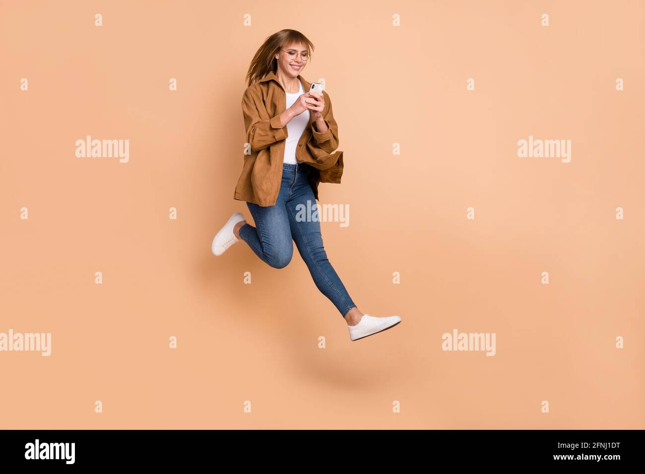 Foto in voller Größe von jungen glücklich lächelnden Mädchen Blogger laufen In Luft süchtig nach Smartphone isoliert auf beigefarbenem Hintergrund Stockfoto