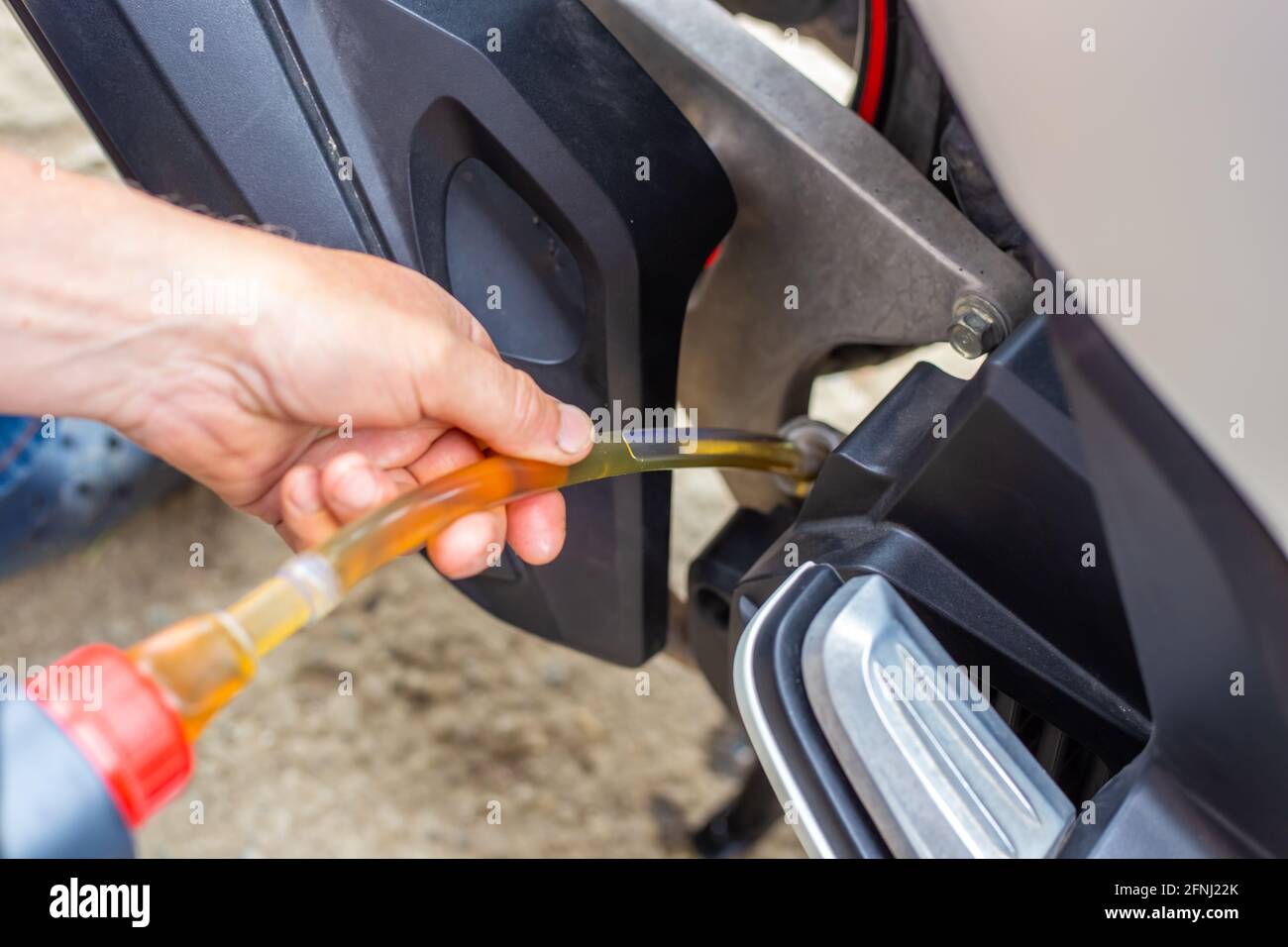 Reparatur und Wartung eines Motorrads. Ölwechsel. Der Automechaniker gießt Öl über einen Gummischlauch in den Motor. Stockfoto