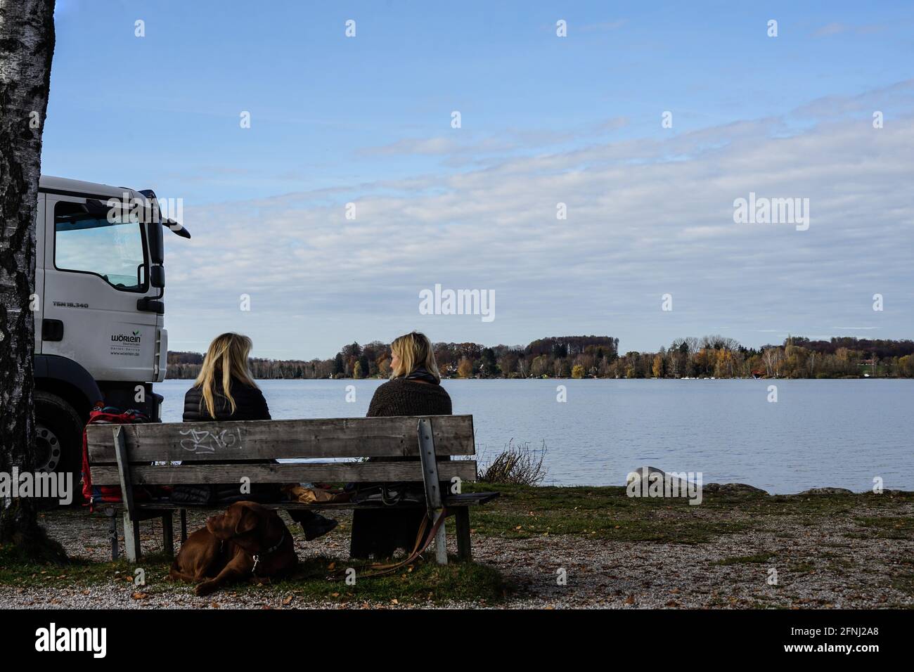 Zwei Frauen sitzen auf einer Bank am See und unterhalten sich. Blick auf den Wörthsee. Das Seeufer ist eine idyllische Umgebung. Stockfoto