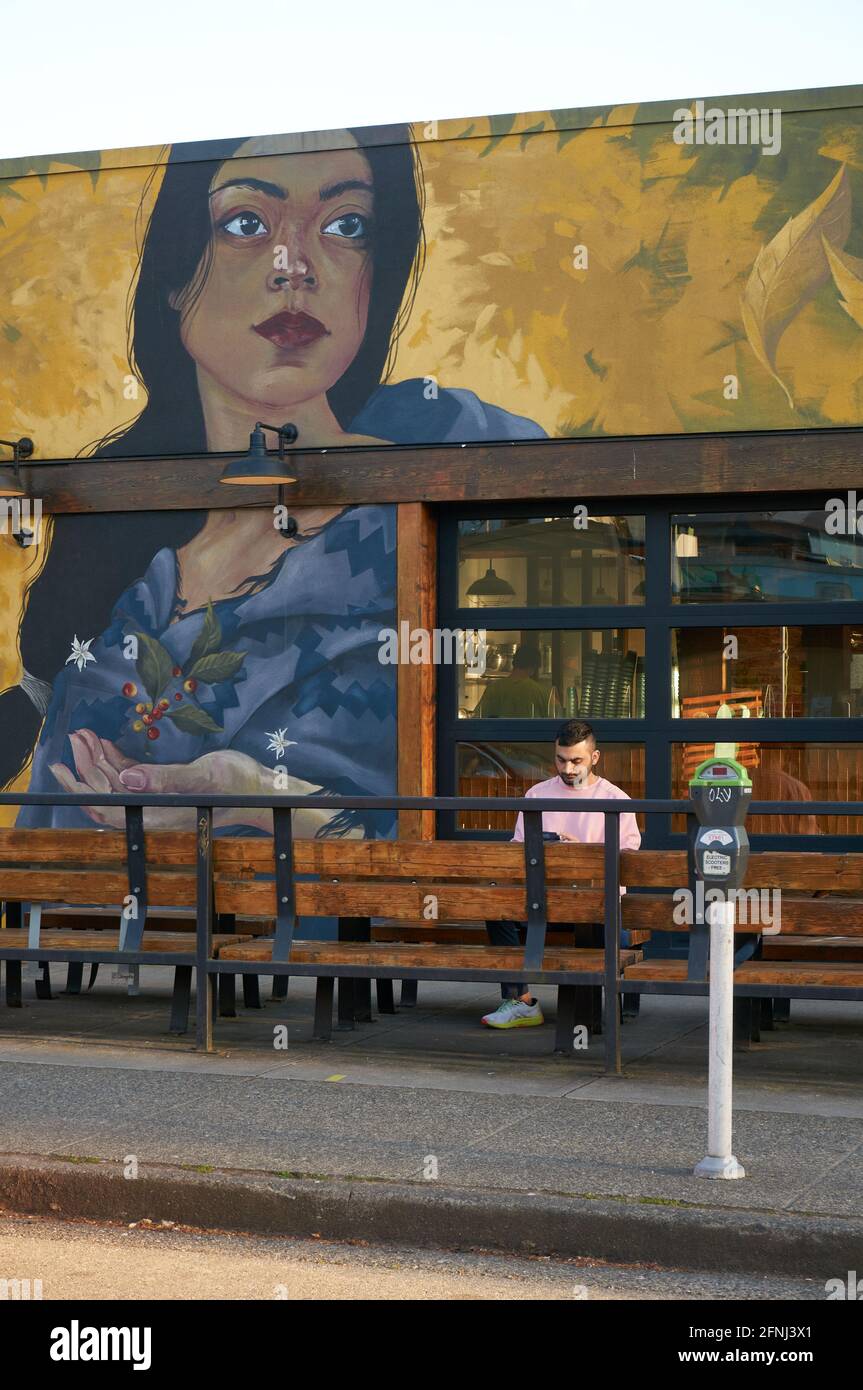 Junger Mann, der vor einem Restaurant an der Main Street in Mount Pleasant, Vancouver, British Columbia, Kanada, sitzt Stockfoto