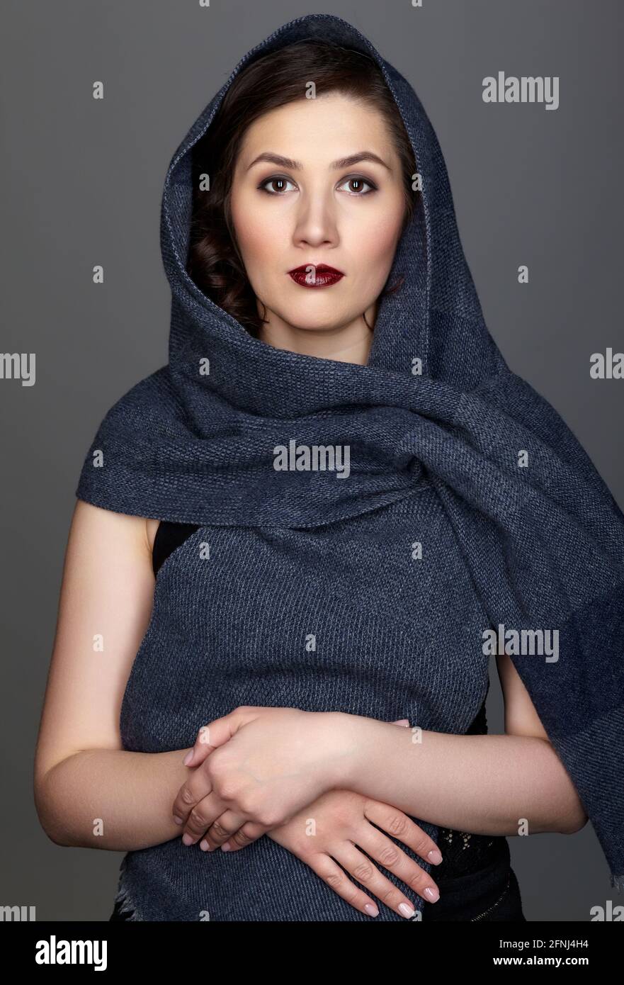 Schönheitsporträt der Brünette Frau in dunkelblauem Schal gekleidet. Weibliches Porträt aus einem Dreiviertel-Winkel auf schwarzem Hintergrund. Der Schal wird von der Hand umwickelt. Stockfoto
