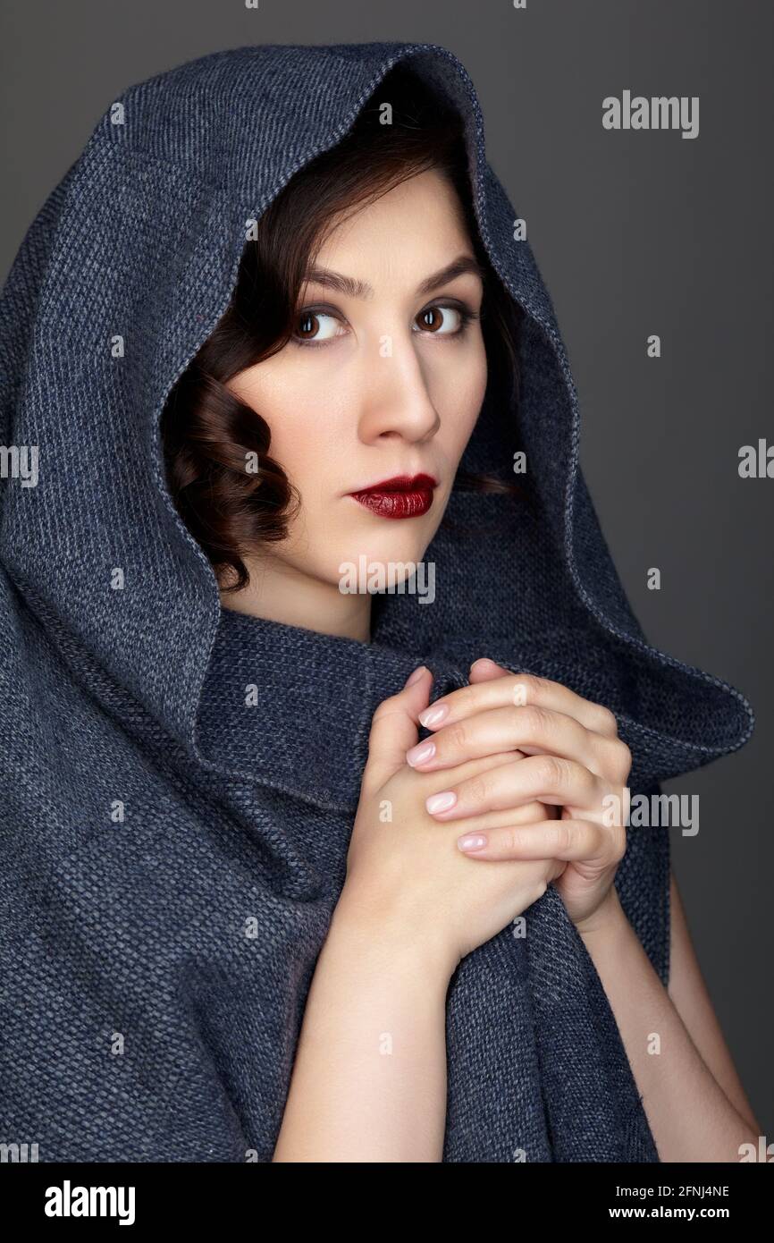 Schönheitsporträt der Brünette Frau in dunkelblauem Schal gekleidet. Weibliches Porträt aus einem Dreiviertel-Winkel auf schwarzem Hintergrund. Der Schal wird von der Hand umwickelt. Stockfoto