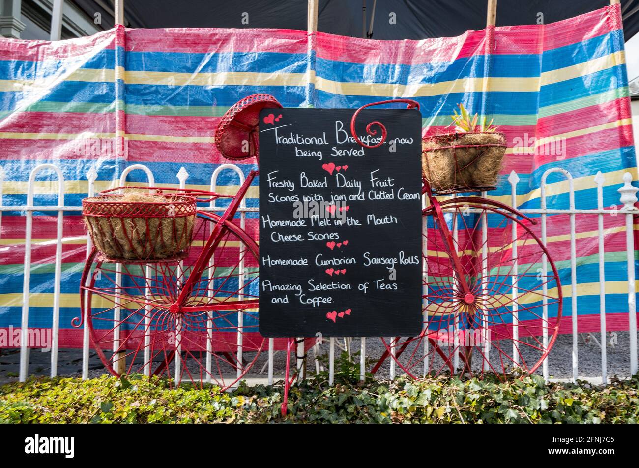 Die Speisekarte des Restaurants Poppi Red steht auf einer Tafel, die an einen rot gestrichenen Zyklus in Hawkshead, Cumbria, England, angeschlossen ist Stockfoto