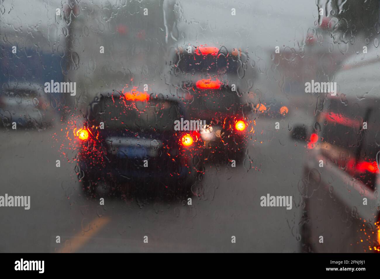 Die Fahrzeuge fahren auf einer regnerisch durchnässten Straße. Die Schlusslichter leuchten in der Dämmerung verschwommen. Stockfoto