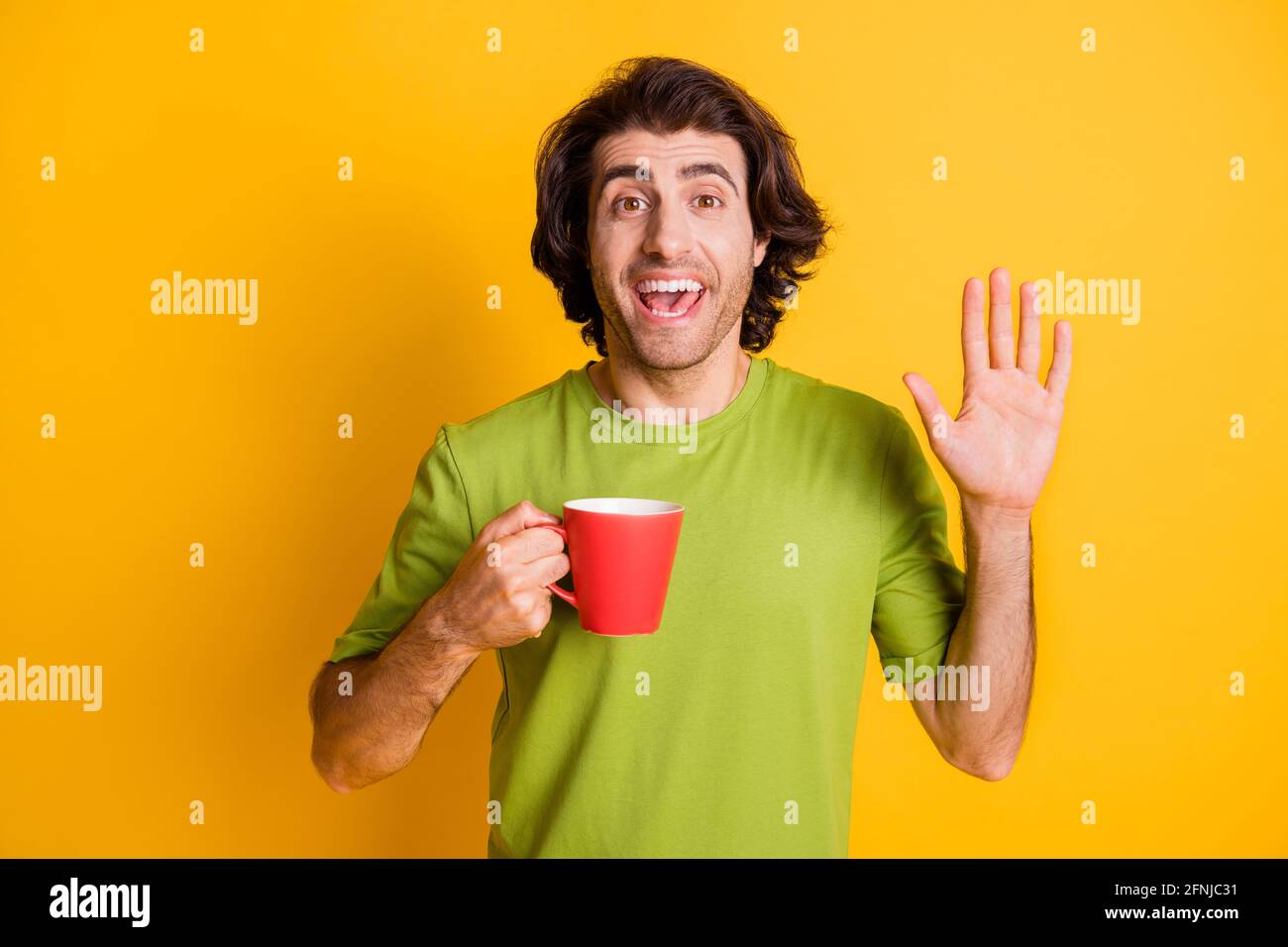 Portraitfoto des Mannes, der eine Tasse Kaffee mit sich winkt Handgruß isoliert auf lebhaft gelbem Hintergrund Stockfoto