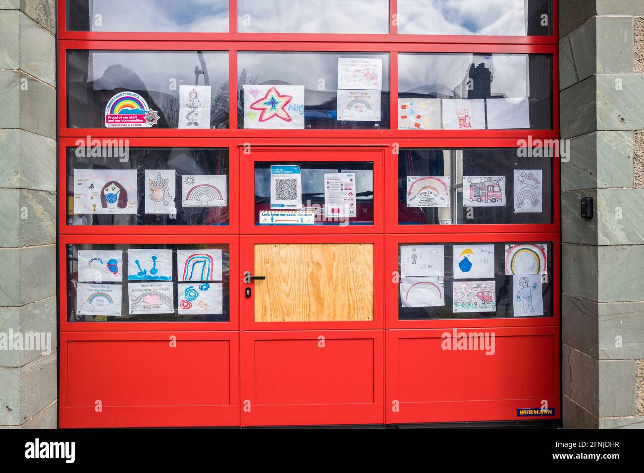 Plakate, die von Kleinkindern angefertigt wurden, um Schlüsselarbeiten und NHS-Mitarbeitern zu danken, wurden an die große rote Tür der Coniston Feuer- und Wiederauferstationsstation angebracht. Stockfoto