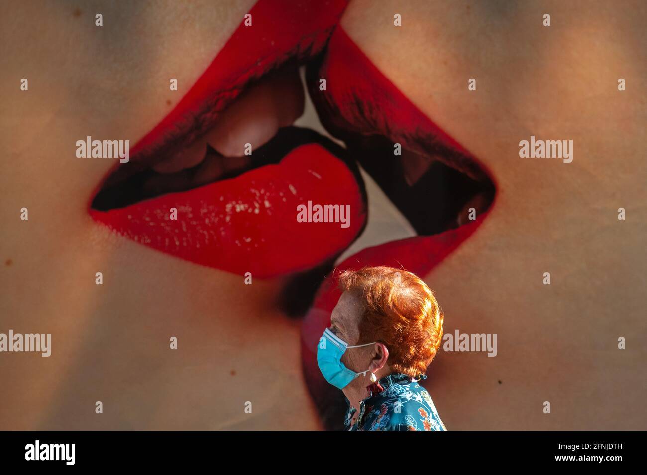 Madrid, Spanien. Mai 2021. Eine Frau, die eine Gesichtsmaske trägt, um die Ausbreitung des Coronavirus (COVID-19) zu stoppen, geht an einer Werbung vorbei, auf der sich zwei Frauen küssen. Fernando Simon, Direktor des Koordinationszentrums für Gesundheitswarnungen und Notfälle des Gesundheitsministeriums, sagte heute auf einer Pressekonferenz: „Wir haben bereits 7.2 Millionen Menschen mit dem vollständigen Zeitplan und mindestens 15 Millionen mit mindestens einer Dosis geimpft. Es ist sehr möglich, dass im Freien, in nicht vielen Tagen, die Verwendung der Gesichtsmaske reduziert werden kann." Quelle: Marcos del Mazo/Alamy Live News Stockfoto