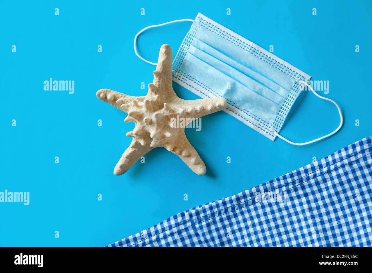 Medizinische Gesichtsmaske neben Strandtuch und Seesternen auf blauem Hintergrund, Draufsicht, Strandartikel und Sommerkonzept Stockfoto