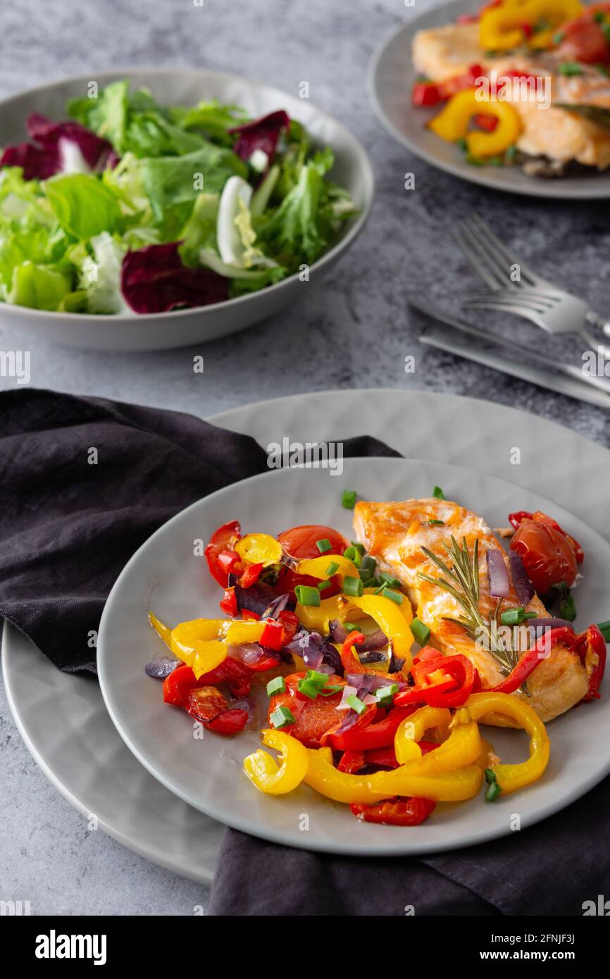 Gebackenes rotes Fischfilet Arctic Saibling auf einem Teller mit Gemüse, Salat in einer Schüssel mischen, leckeres herzhaftes gesundes Abendessen Stockfoto