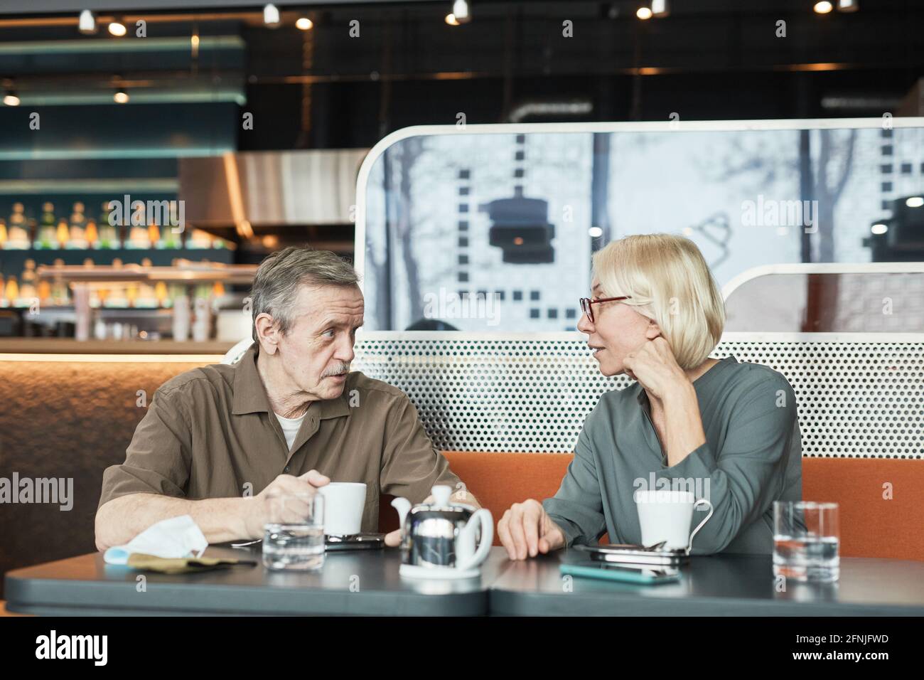 Reifer Mann mit Schnurrbart sitzt am Tisch und erzählt Geschichte An neugierige Freundin, während sie Tee im Café trinken Stockfoto