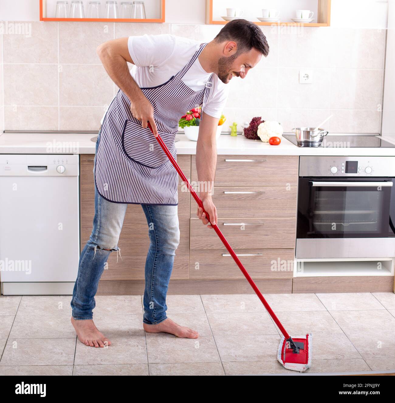 Schöner Kerl wischen Küchenboden vor den Schränken und Arbeitsplatte zu Hause Stockfoto