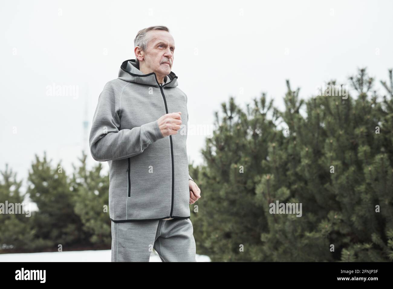 Seriöse ältere kaukasische Mann in grauem Sportanzug schwingende Arme Beim Laufen allein im Wald Stockfoto