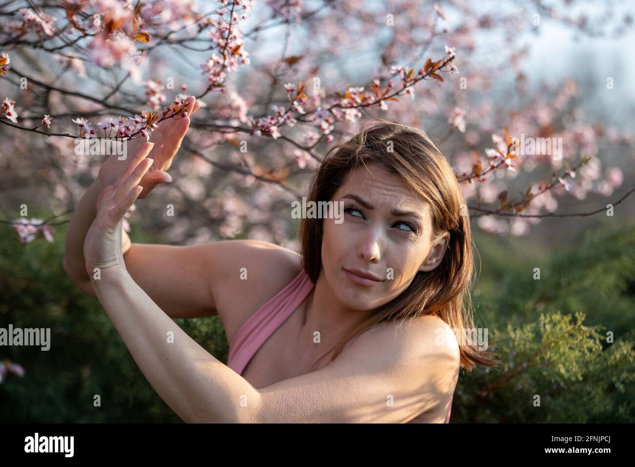 Ängstlich junge Frau, die auf blühenden Baum schaut und Stoppschild mit Palmen zeigt. Frühjahrsallergie-Angriffskonzept Stockfoto