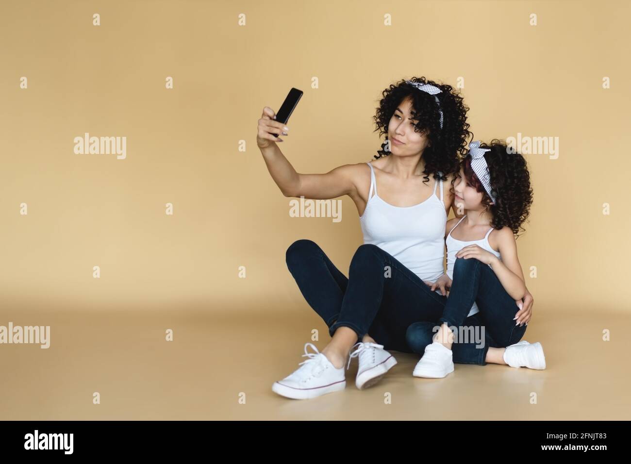 Junge Mutter und kleine Tochter sitzen auf dem Boden und machen Selfie. Stockfoto