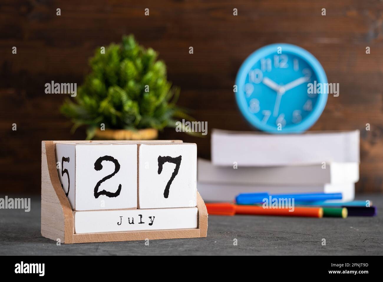Juli. Juli 27 Holzwürfelkalender mit unscharfen Objekten auf dem Hintergrund. Stockfoto