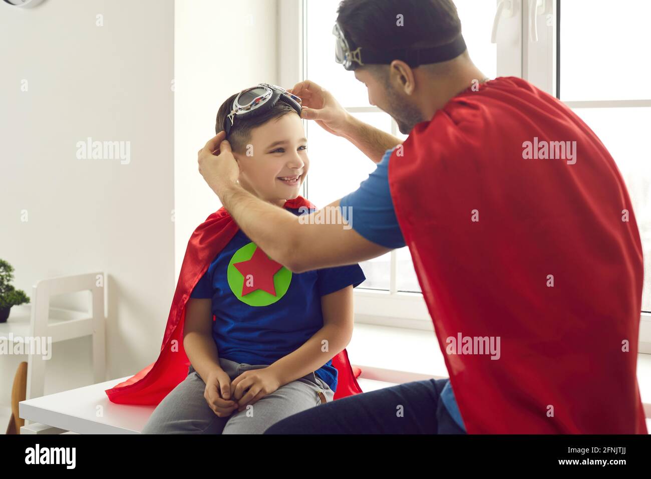 Papa hilft dem kleinen Sohn, beim Spielen eine Pilotenbrille zu tragen Spaß Superhelden Spiele zusammen Stockfoto
