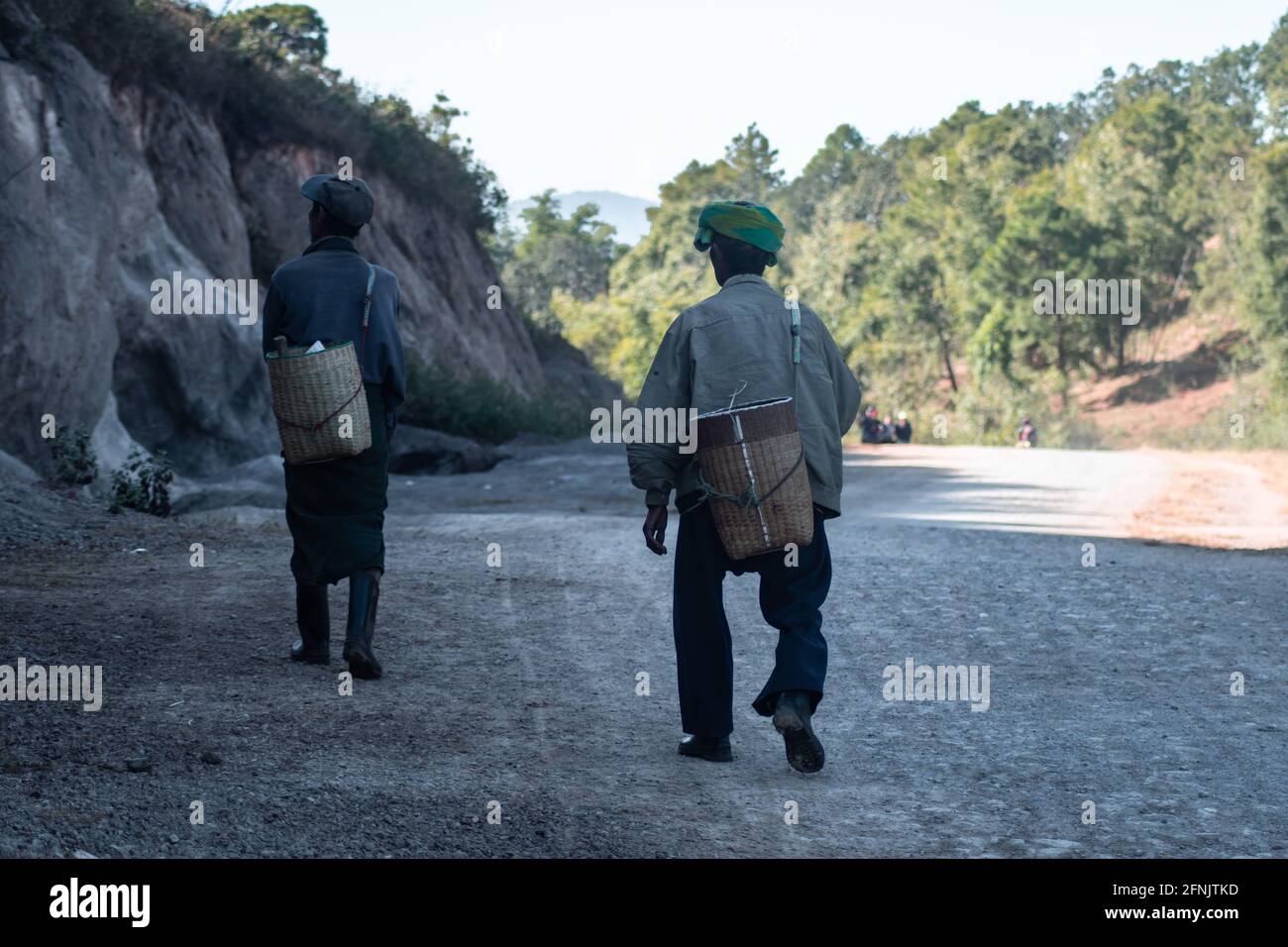 Zwei burmesische Männer tragen einen Korb, während sie auf einer Schotterstraße zwischen Kalaw und Inle Lake, Shan State, Myanmar, spazieren Stockfoto