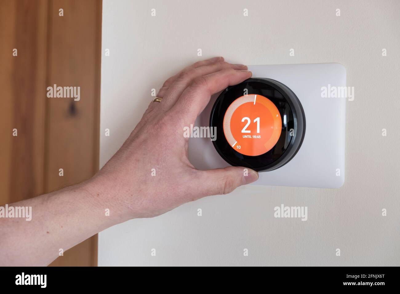 Person, die einen intelligenten Thermostat in einem vernetzten Smart Home steuert Stockfoto