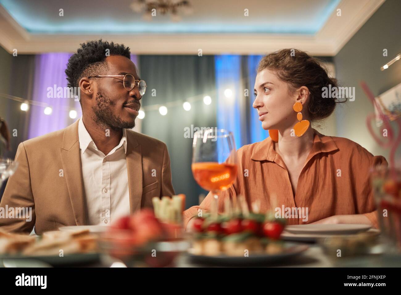 Porträt eines eleganten Paares mit gemischter Rasse, das mit Freunden im Haus zu Abend gegessen hat Und einander anschauen Stockfoto