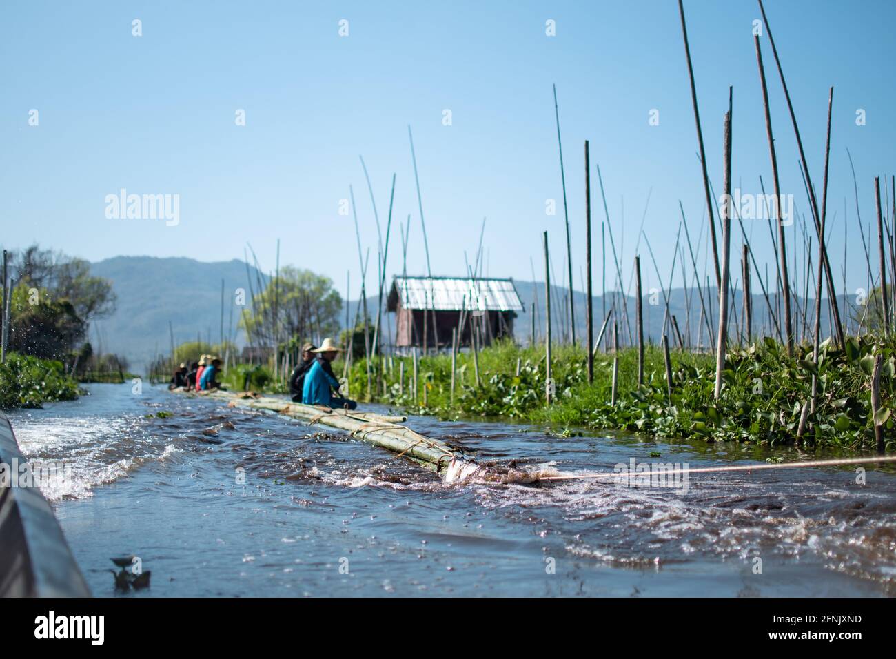 Shan State, Myanmar - Januar 7 2020: Einheimische sitzen auf Bambus und schweben auf einem Fluss, der von einem Boot am Inle Lake, Nyaung Shwe, gezerrt wird Stockfoto