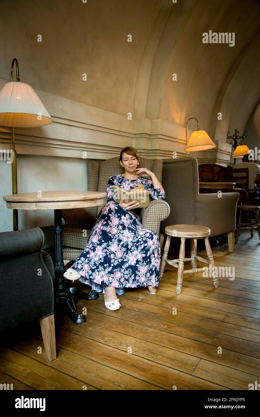 Schöne Frau mit einem Buch in ihren Händen. Eine Frau sitzt in einem gemütlichen Café, liest und trinkt Kaffee. Stockfoto
