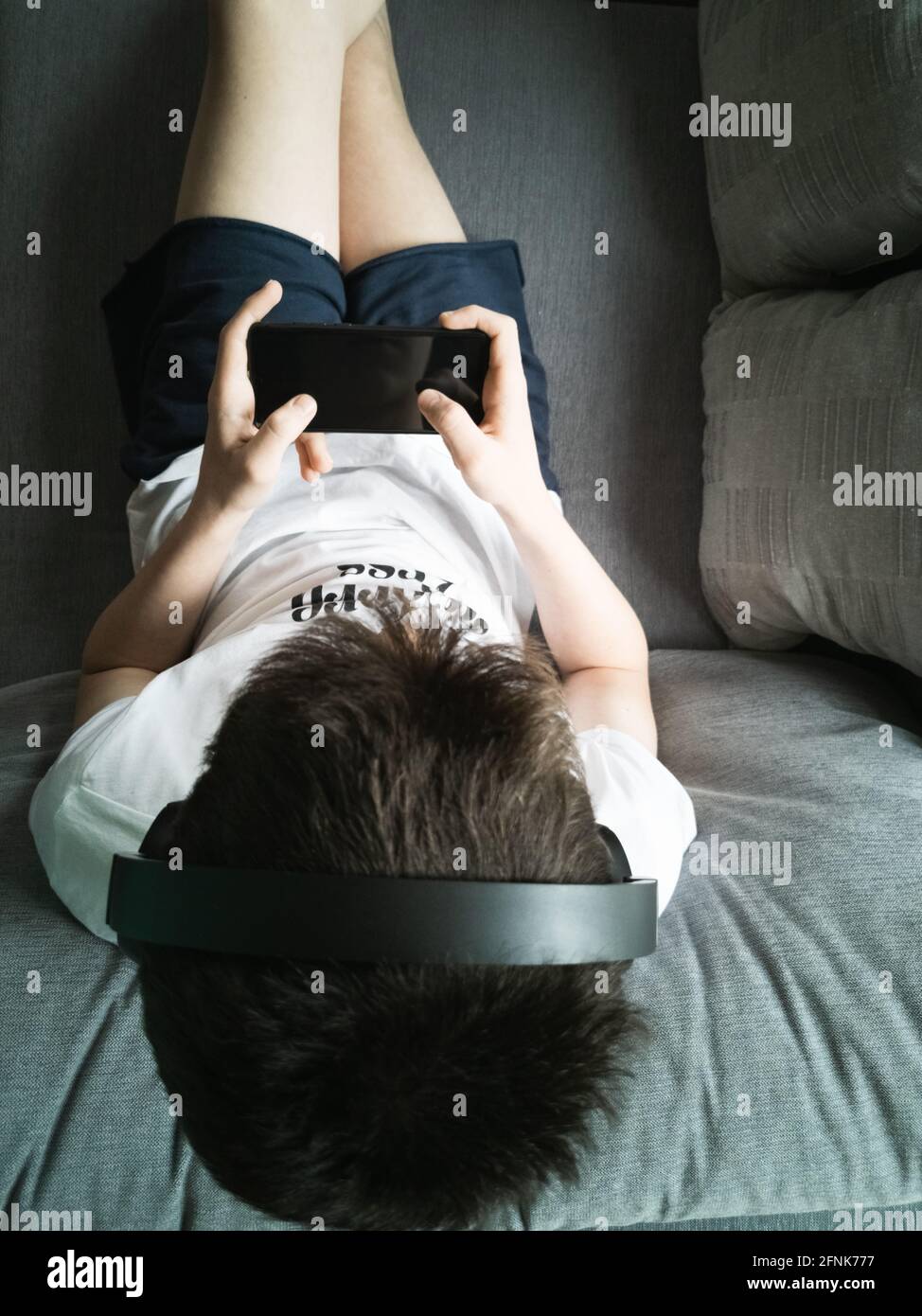 Junge 15 Jahre alt sitzt auf dem Sofa in Kopfhörer Mit einem Smartphone Stockfoto