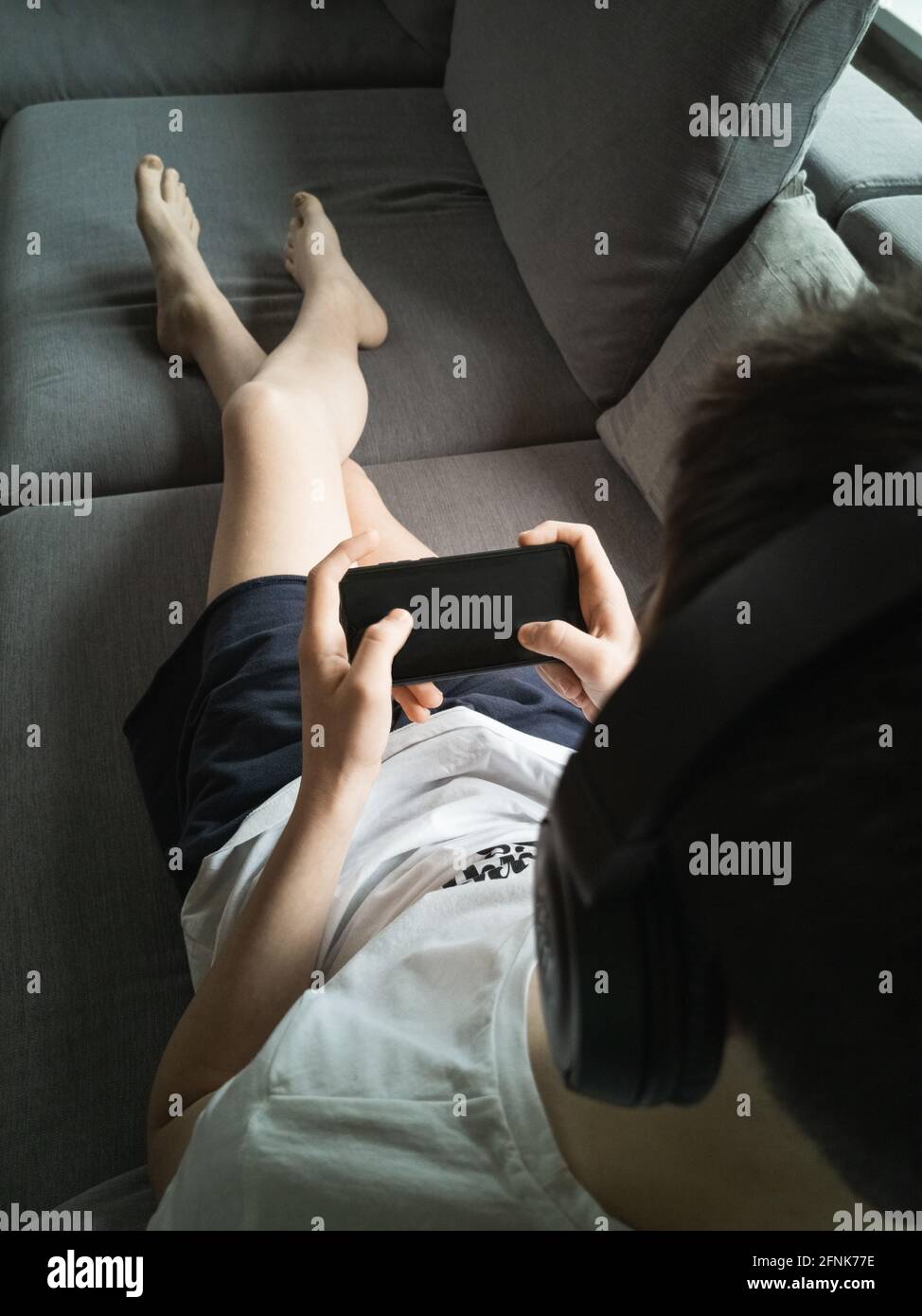 Junge 13-15 Jahre alt auf der Couch mit einem Smartphone In seinen Händen Stockfoto