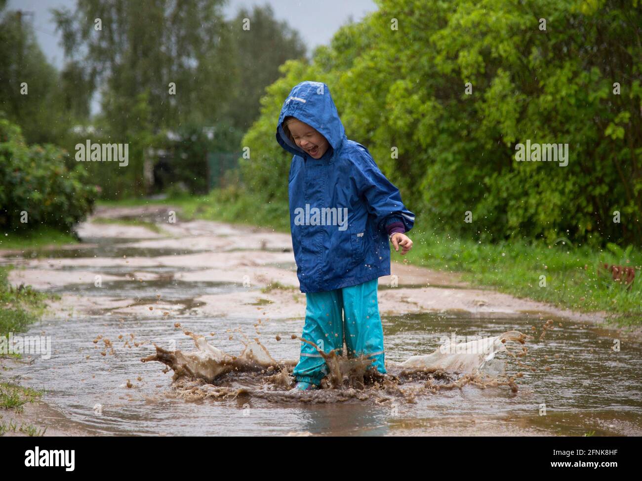 Glückliches Kind springt in eine Pfütze. Stockfoto