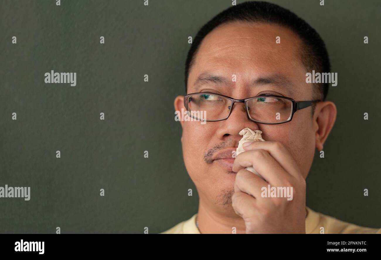 Asiatischer Mann mit Serviette in der Nase, um den Snot zu stoppen, langweilige Gesicht, Blick zur Seite. Stockfoto