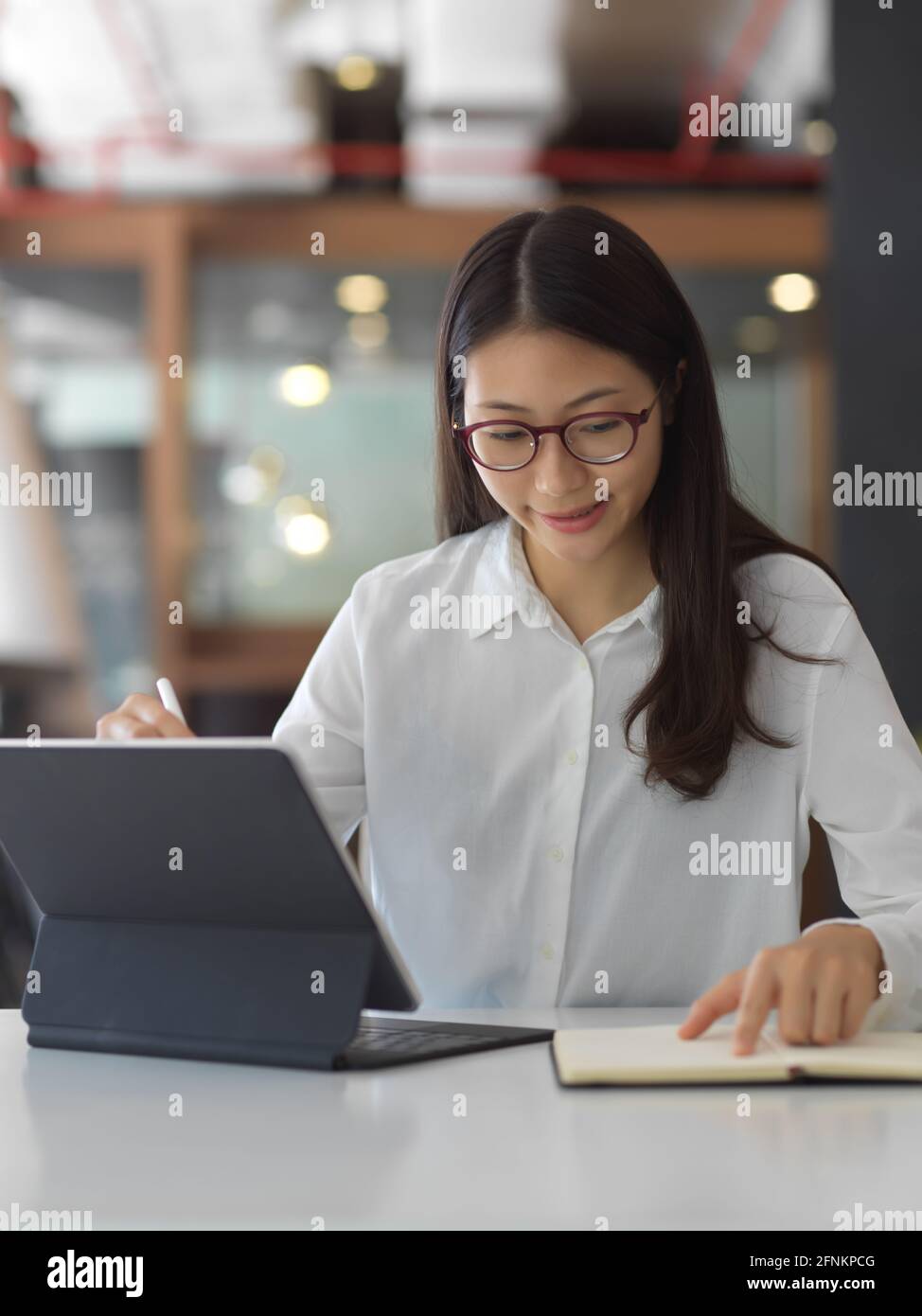 Porträt einer Frau, die während der Arbeit mit Digital auf einem Notebook wringen soll Tablet im Bürozimmer Stockfoto