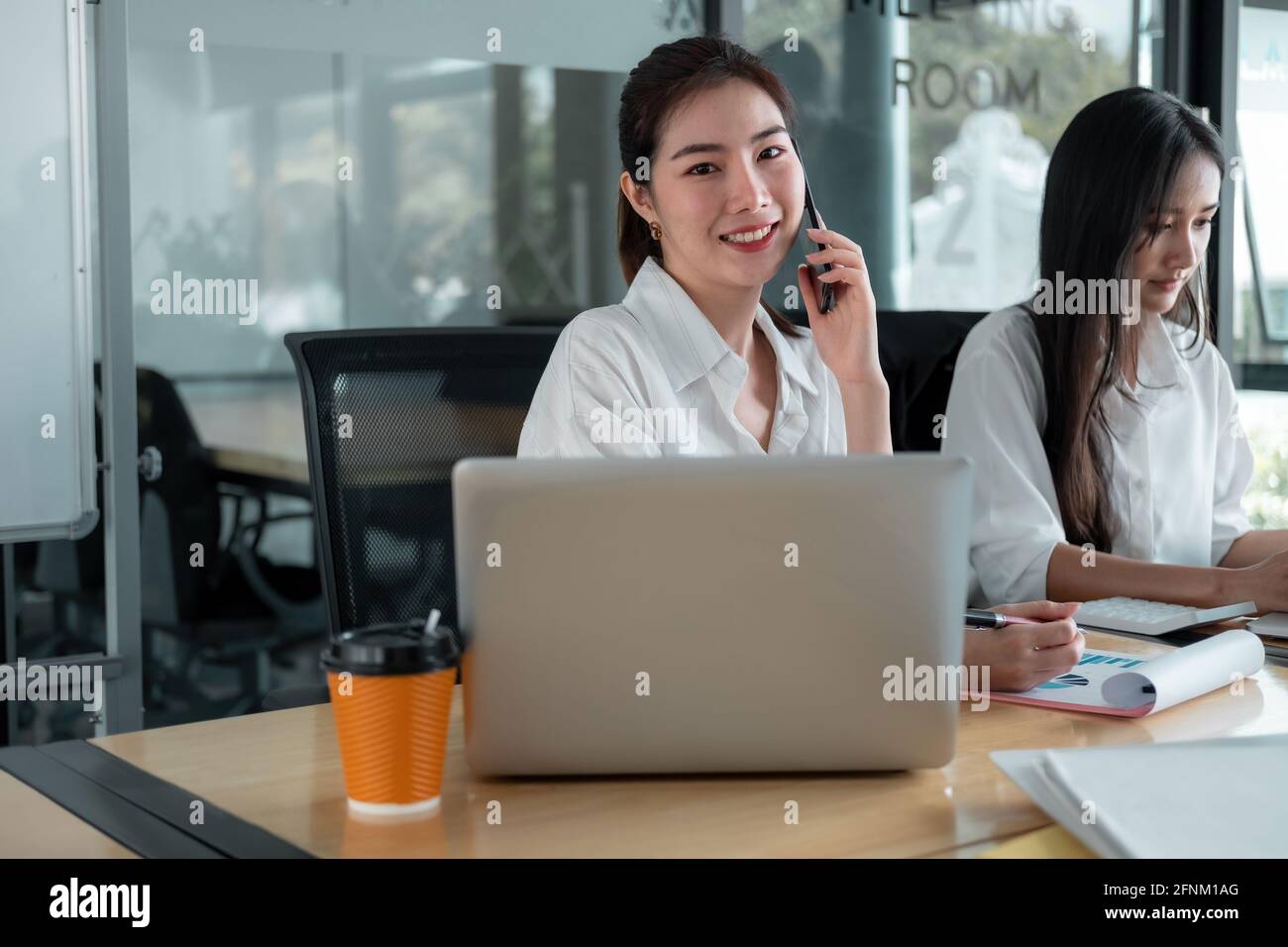 Porträt einer attraktiven asiatischen Geschäftsfrau, die während eines Telefonanrufs am Laptop für die Planung der Geschäftsstrategie arbeitet. Stockfoto