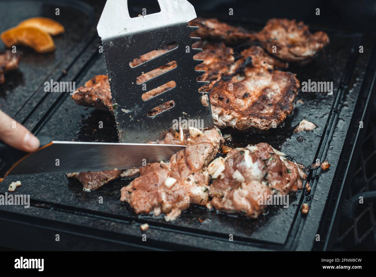 Der Mann schneidet einen Schweinehals, duftend und reich gewürzt mit Basilikum, Pfeffer, Salz und anderen Kräutern, der auf einer Granitplatte über einem offenen Feuer gebraten wird. Foo Stockfoto