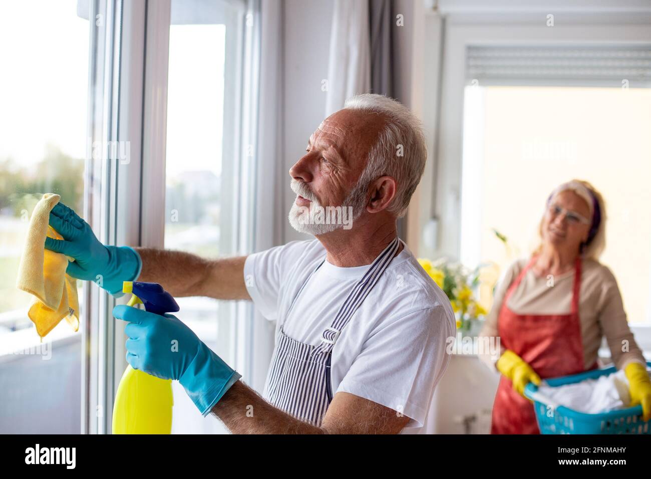 Älterer Mann, der die Fenster putzt und eine Frau, die zu Hause ihre Wäsche wäschet Stockfoto