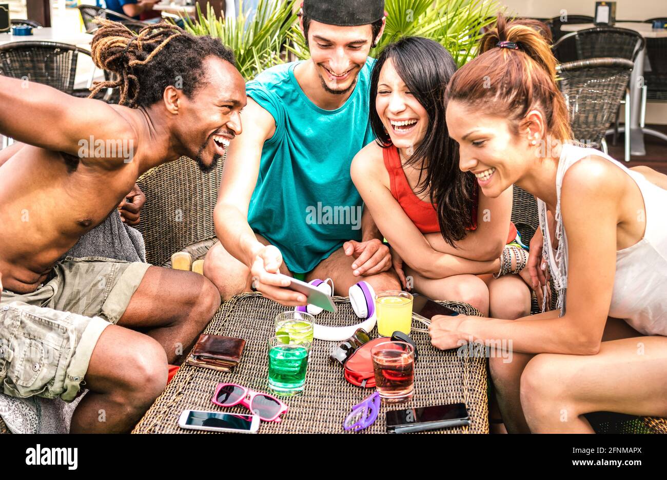Multirassische Freunde, die am Strand Spaß mit dem Handy haben Cocktailbar – Junge, glückliche Menschen, die mit dem Smartphone süchtig sind Stockfoto
