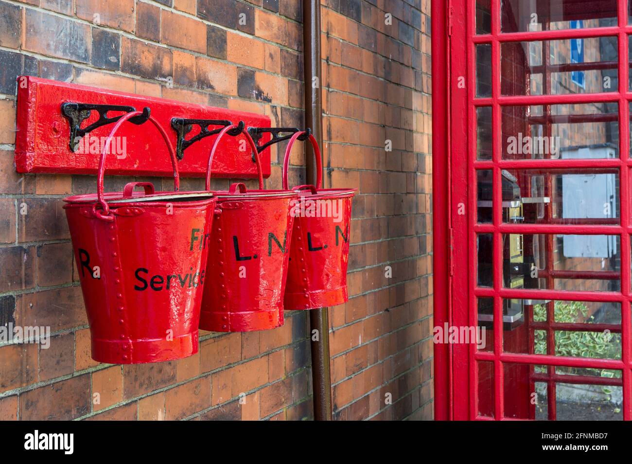 Drei rote Feuereimer gegen einen roten Telefonkiosks auf dem Bahnsteig am Bahnhof Quorn & Woodhouse, Great Central Railway, Großbritannien Stockfoto