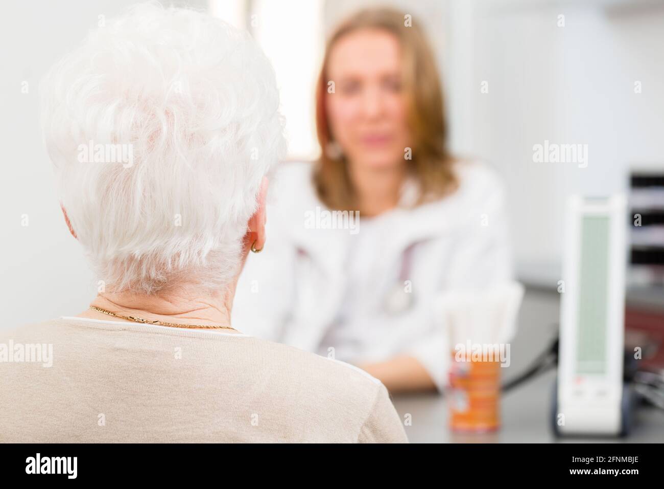 Junge Ärztin mit Rentner in Chirurgie Sprechstunde am Schreibtisch saß Stockfoto