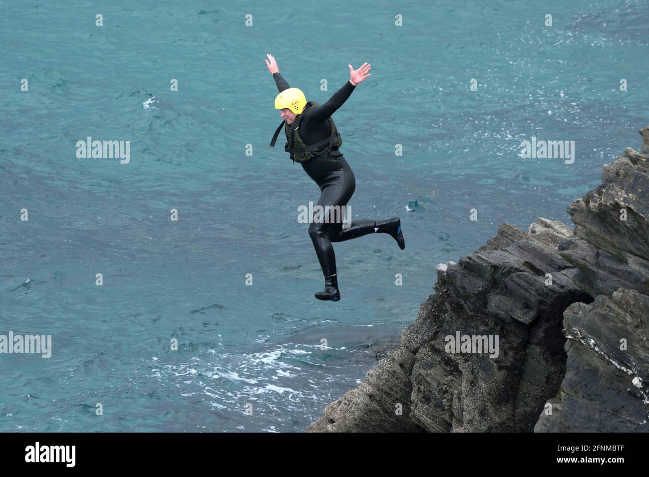 Ein koaSteering Urlauber, der von Felsen ins Meer springt, auf einer koaSteering Reise um Towan Head in Newquay in Cornwall. Stockfoto