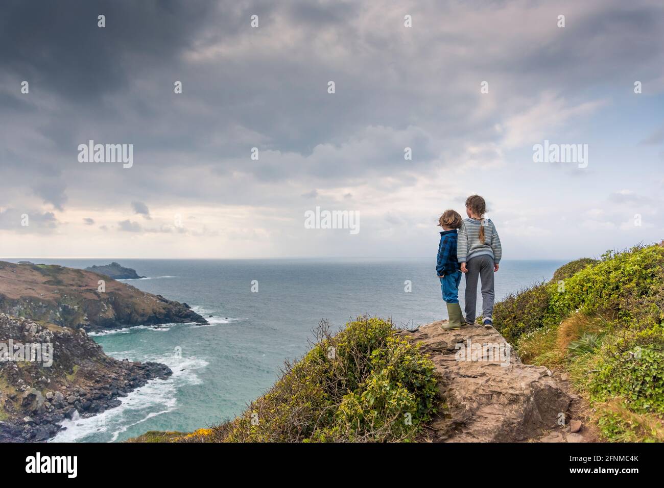 Zwei Kinder stehen auf Zennor Head und blicken über das Meer nach Gurnard’s Head an der Küste von West Penwith in Cornwall. Stockfoto