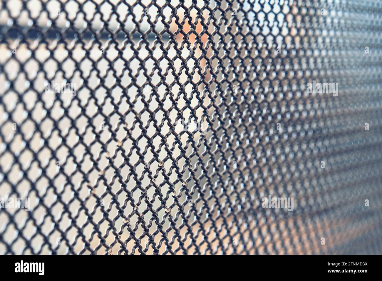 Dunkles Metallzaungitter mit Muster von zahlreichen kleinen geformt Zellen auf hellem unscharfem Hintergrund installiert extreme Nahansicht Stockfoto