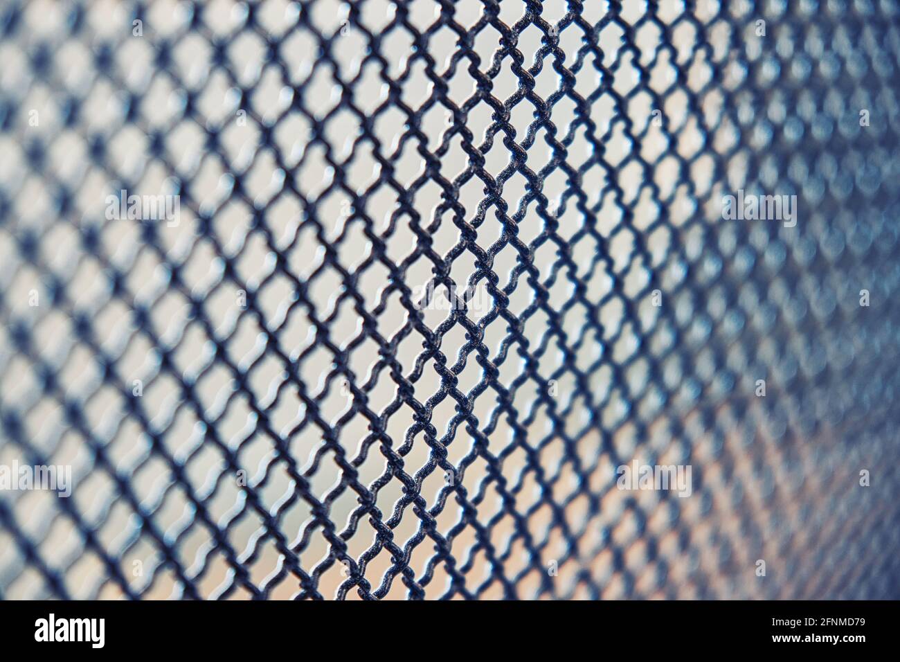 Dunkles Metallzaungitter mit Muster von zahlreichen kleinen geformt Zellen auf hellem unscharfem Hintergrund installiert extreme Nahansicht Stockfoto