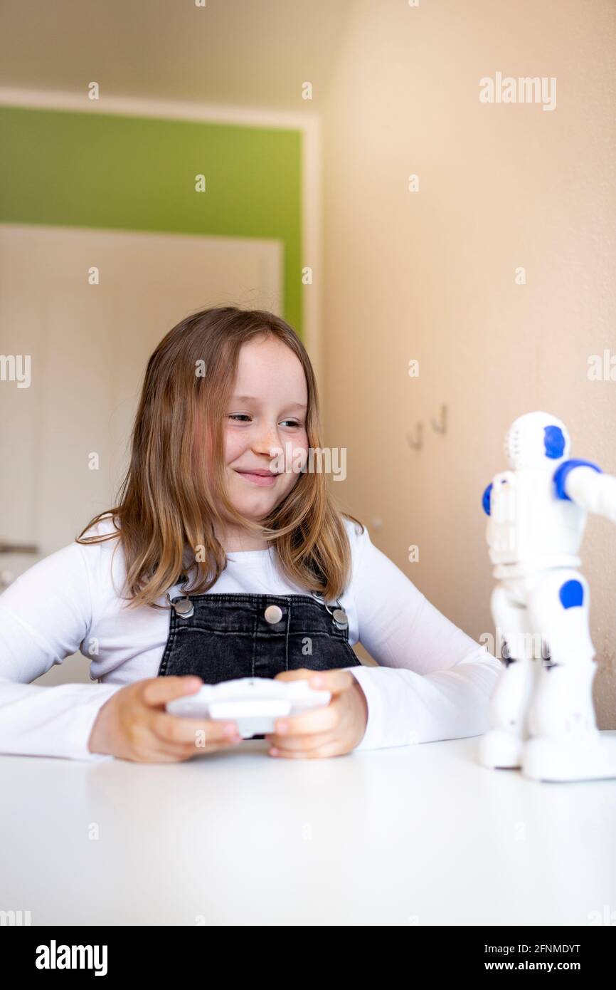 Ziemlich junges Schulmädchen, das auf ihrem Schreibtisch in ihrem Zimmer  sitzt Zu Hause spielt während der Corona-Zeit mit einem kleinen Roboter  Stockfotografie - Alamy