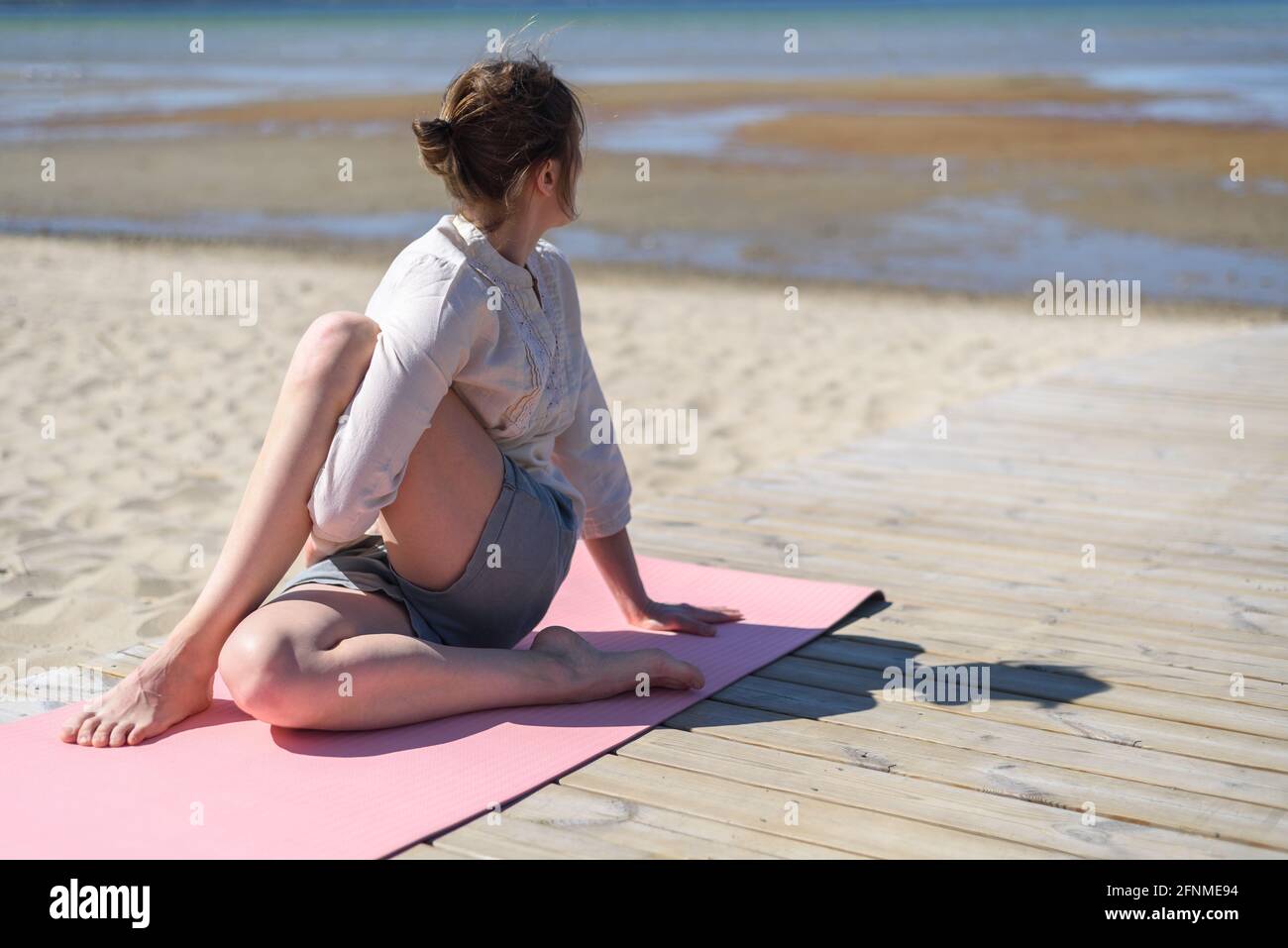 Frau in Leinenkleidung macht Yoga-Stretch-Pose am Strand an sonnigen Tag. Wohlbefinden, körperliche und geistige Gesundheit Stockfoto